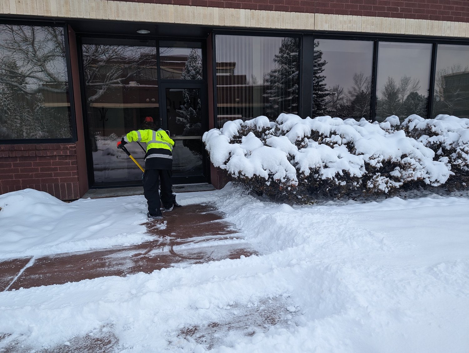 crew removing snow on sidewalk by front door of commercial business