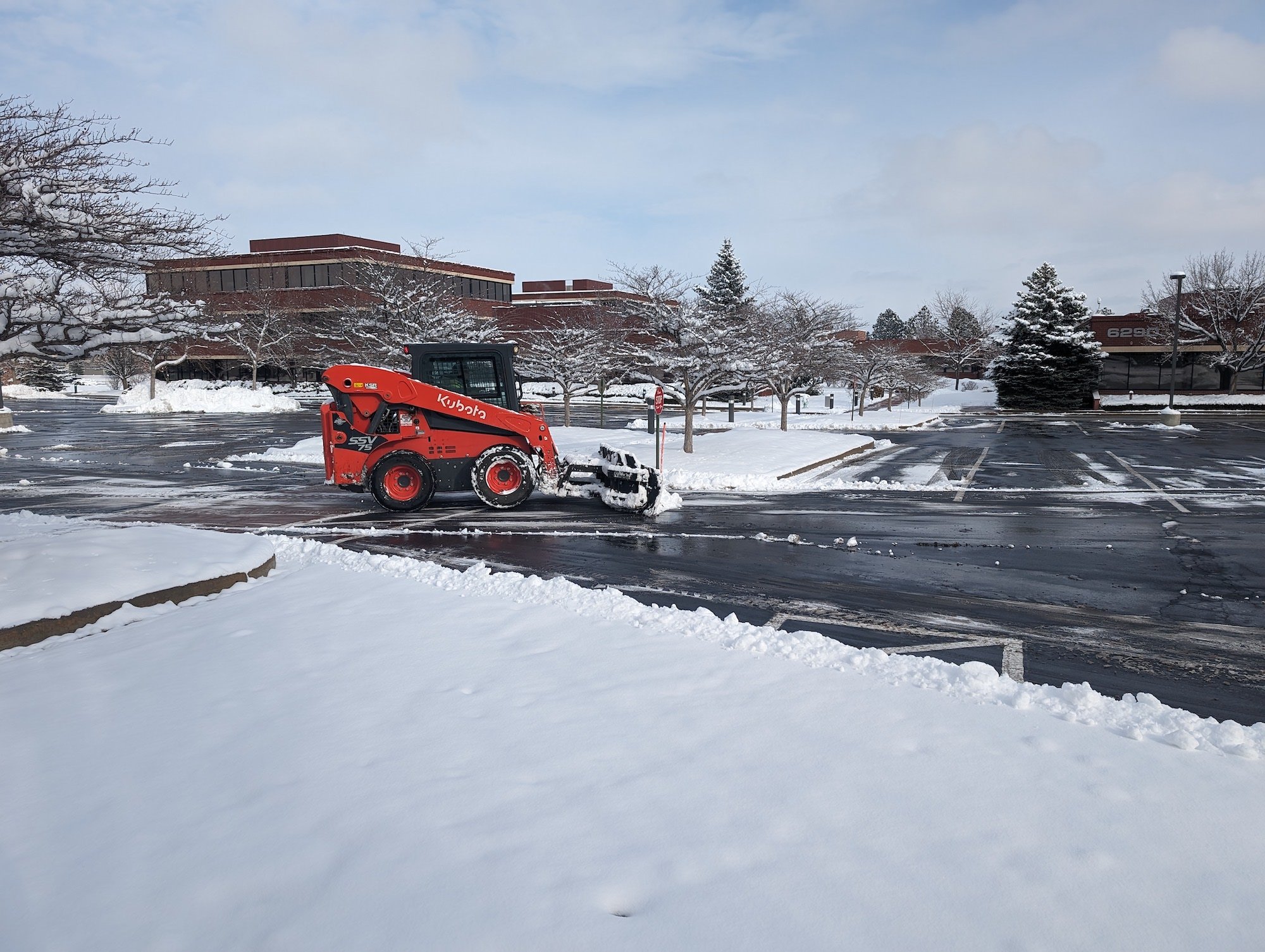 red snow plow removing snow from commercial parking lot 