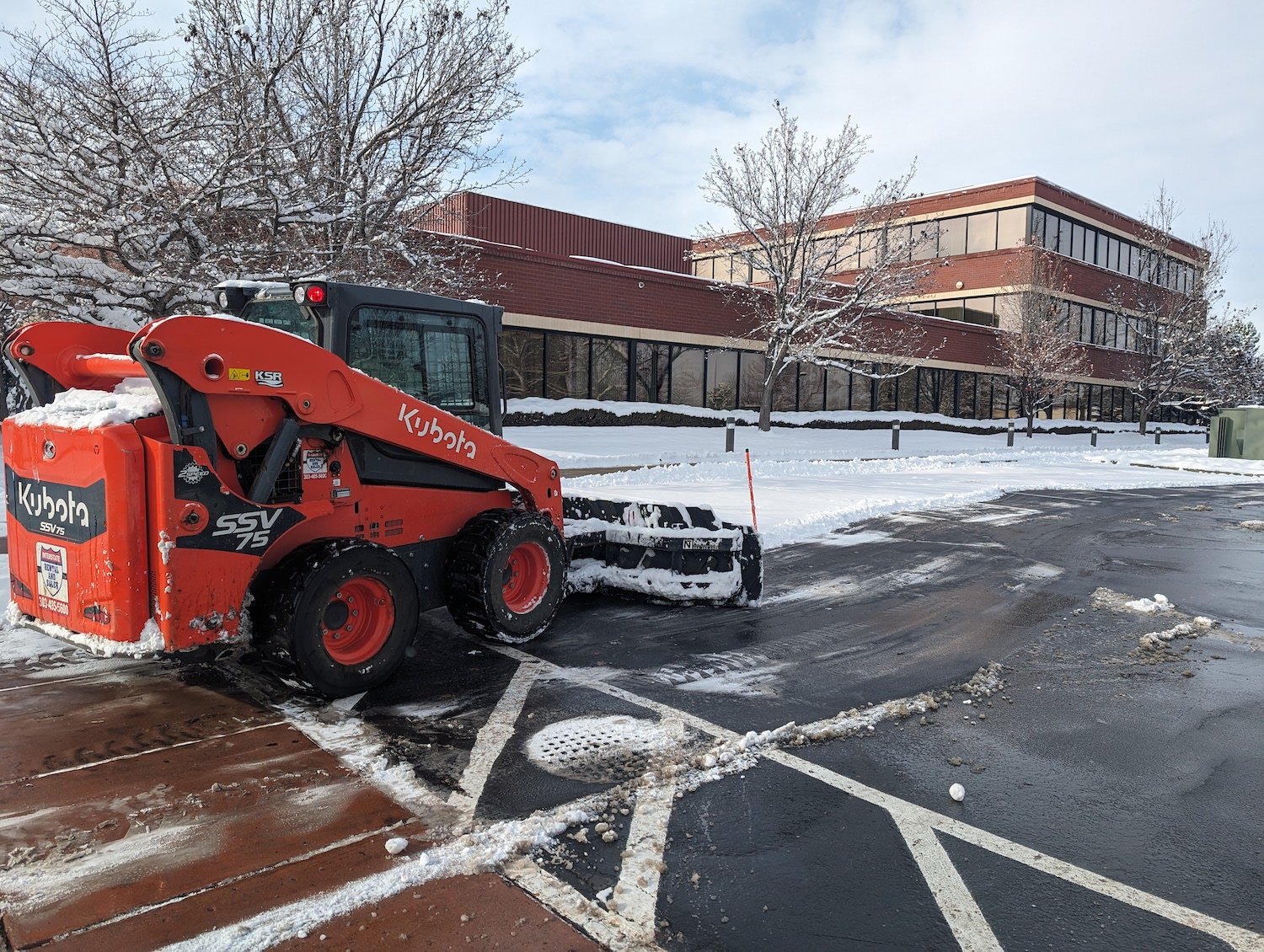 red snow plow removing snow in front of commercial business