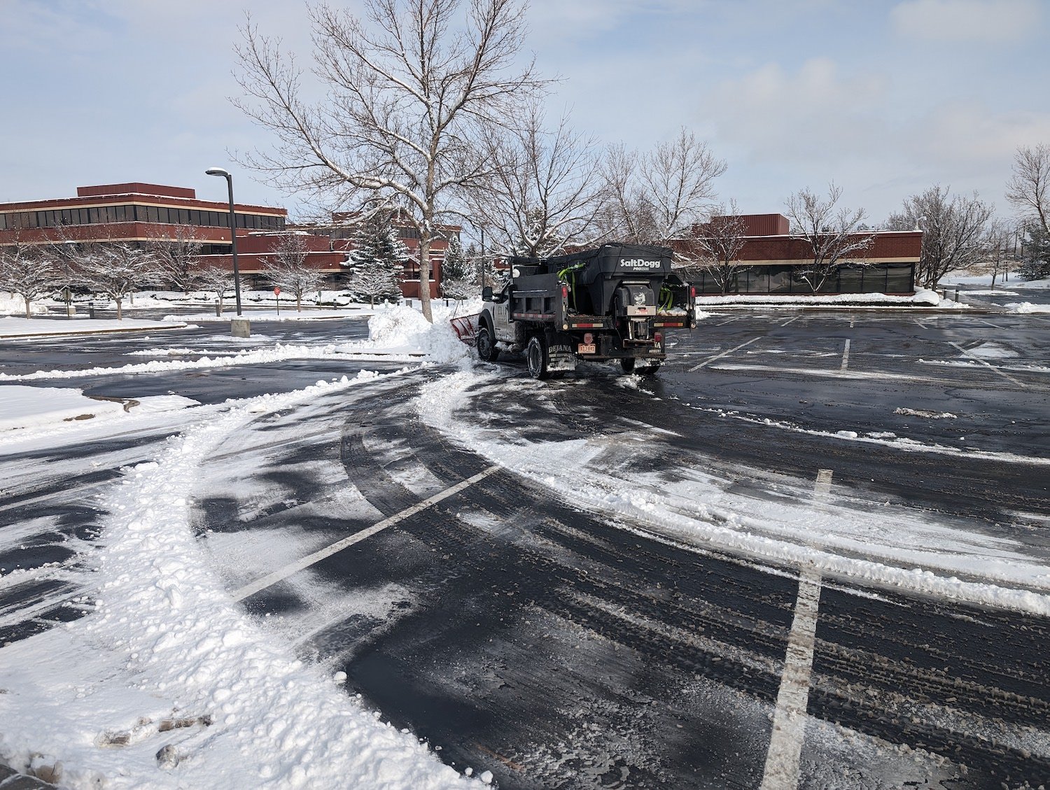 snow plow truck removing snow from parking lot and salting